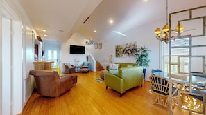 A spacious living area with a wooden floor, a green sofa, a brown armchair, a dining table with chairs, and a staircase leading to an upper level. - A Pineapple Paradise (Bolivar Peninsula)