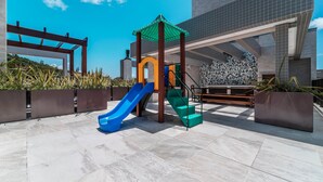 Un’area giochi con scivoli e una struttura per arrampicarsi, circondata da un edificio moderno con piastrelle decorate.