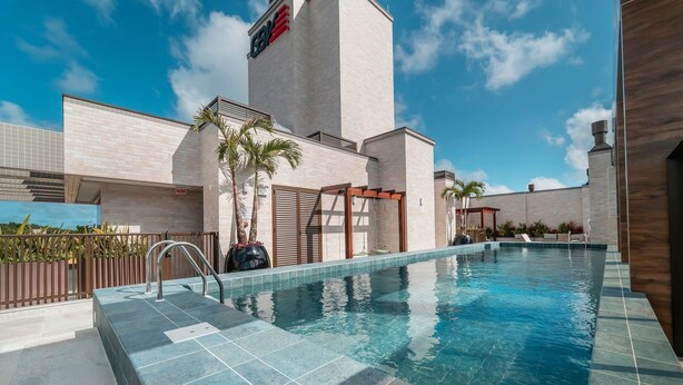 Una piscina con acqua cristallina e blu, circondata da un solarium piastrellato e un pergolato.