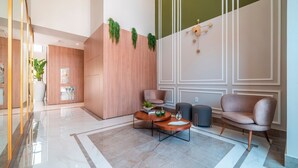 Una hall moderna con pavimento in marmo lucido, pareti rivestite in legno e un’area salotto con un tavolino rotondo e due sedie.