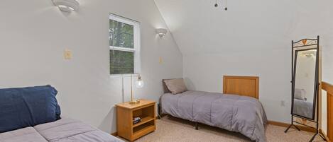 A bedroom with two single beds, a nightstand with a lamp, a mirror, and a window with blinds.