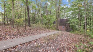 Ein rustikales Blockhaus, umgeben von einem Wald, mit einem Betonweg davor.
