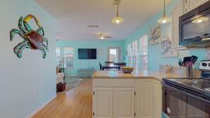 Una cocina con una isla central, un comedor con sillas, un ventilador de techo y un televisor montado en la pared.