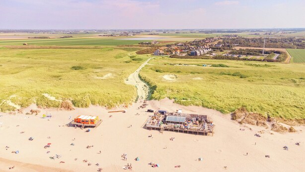Een strand met een zandrijk strand, een houten steiger en een klein gebouw.