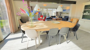 Een moderne eetruimte met een houten tafel en stoelen, een bloevas en uitzicht op het landschap door grote ramen.