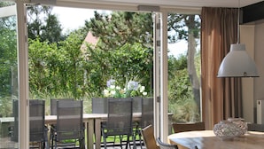 Een buiten eetgedeelte met een glazen deur naar een tuin, met een tafel, stoelen, een lamp en een decoratieve schaal.