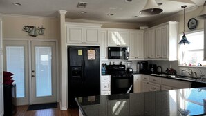 A kitchen with white cabinets, a black refrigerator, a microwave, and a large island with a black countertop. - La Casa Bonita: 2  BR, 2  BA House in Crystal beach, Sleeps 8 (Bolivar Peninsula)