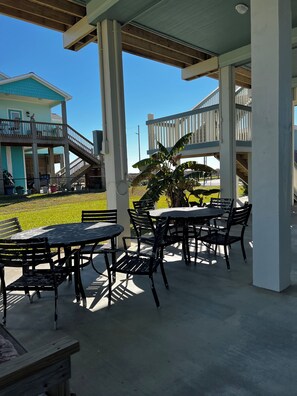 Eine überdachte Terrasse im Freien mit Tischen und Stühlen, eine Holzterrasse und im Hintergrund ein Haus.