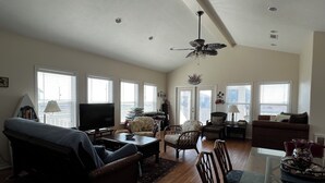 A spacious living room with a ceiling fan, a television, and a dining area with a glass table. - La Casa Bonita: 2  BR, 2  BA House in Crystal beach, Sleeps 8 (Bolivar Peninsula)
