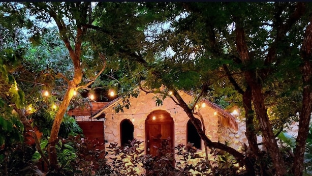 A circular outdoor seating area with cushions, a stone fire pit, and string lights. - This home features lush garden & private pool. (Isla mujeres)