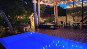 An outdoor pool area with a wooden deck, lounge chairs, and a pergola with string lights. - This home features lush garden & private pool. (Isla mujeres)