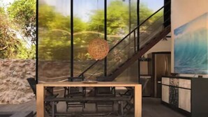 A modern interior with a wooden table, a staircase, and a large window with a view of greenery. - This home features lush garden & private pool. (Isla mujeres)