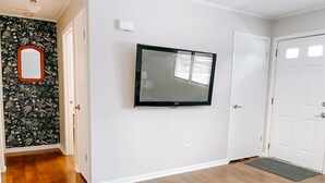 A hallway with a wooden floor, a wall-mounted TV, a door, and a doorbell.