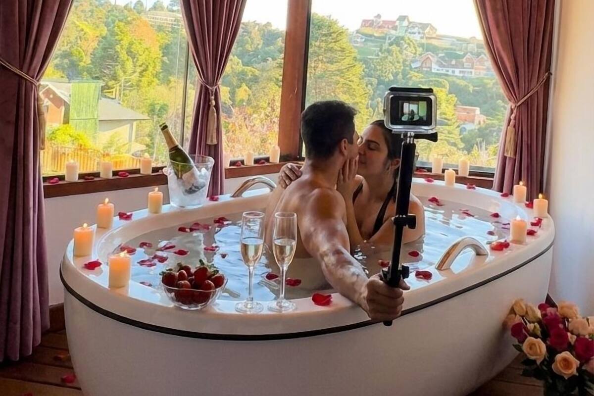Een koppel in een jacuzzi, met een camera op een statief, omringd door kaarsen en rozenblaadjes.