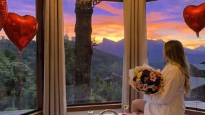 A room with a large bathtub filled with bubbles, a chandelier, and a view of mountains at sunset. - Pousada Recanto dos Moinhos (Campos do Jordão)