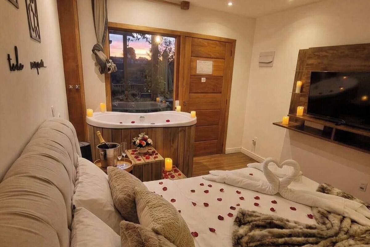 Een hotelkamer met een bed versierd met rozenblaadjes en een zwaan-vormig kussen, een houten deur, een klein tafeltje met kaarsen, en een aan de muur bevestigde televisie.