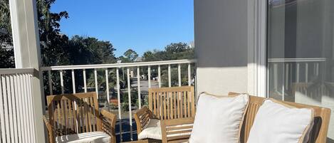 A balcony with wooden furniture, including a sofa and chairs, and a patterned rug.