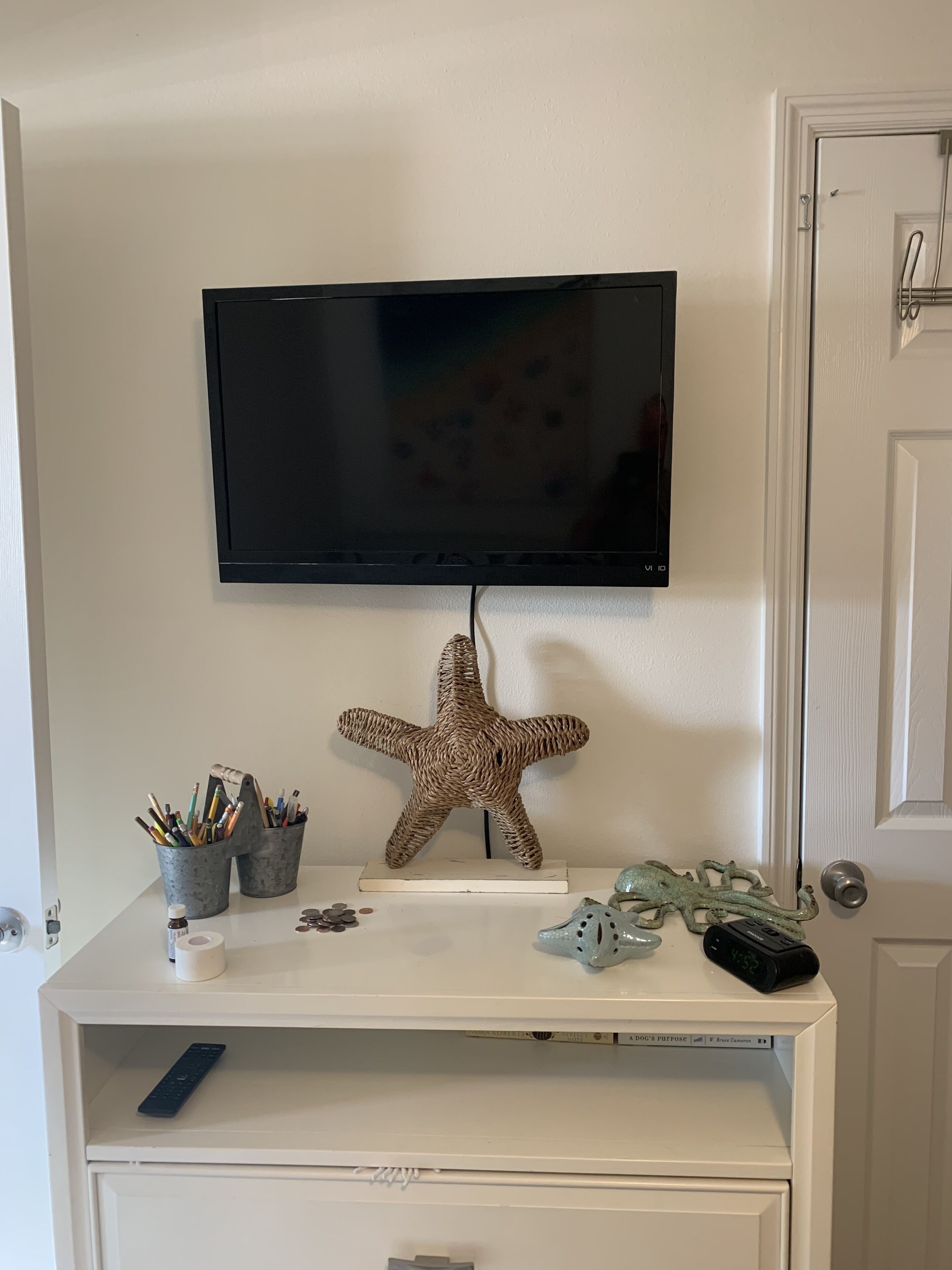 A white entertainment unit with a mounted TV, a starfish decoration, and a remote control.
