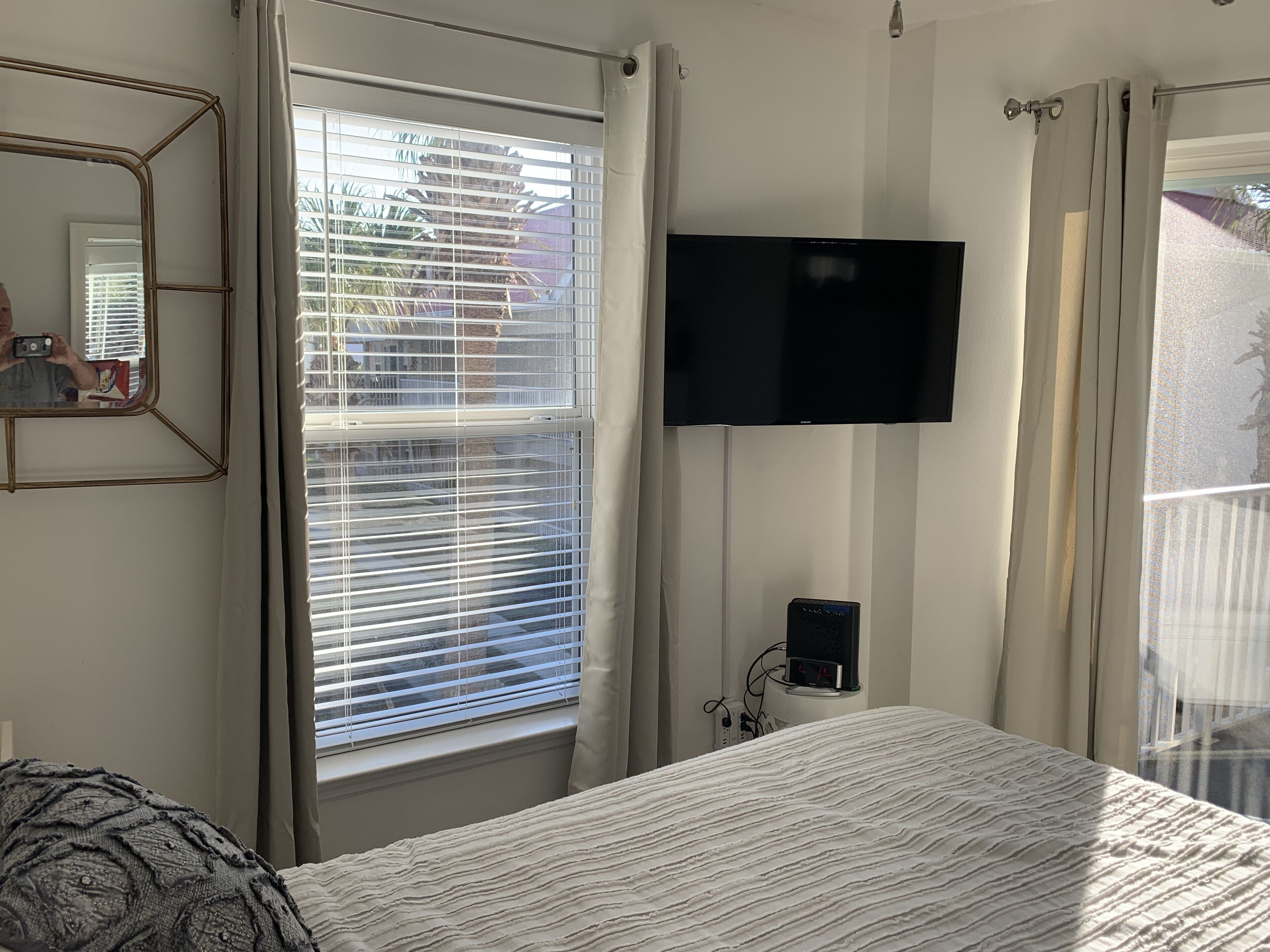 A hotel room with a bed, a TV mounted on the wall, and a window with blinds.