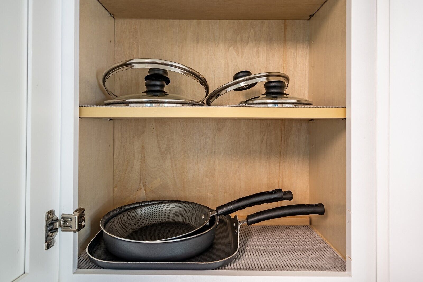 Un armario de cocina con dos ollas de acero inoxidable en el estante superior y una sartén negra en el inferior.