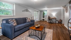 A living room with a blue sofa, a wooden coffee table, and a desk with a chair. There is a plant on the desk, a rug on the floor, and a wall clock. - Marietta! Near the Square, Pets & Long stays ok. Entire home (Marietta)