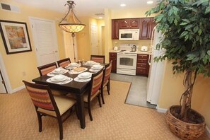 A dining area with a table set for six, a microwave, oven, and a potted plant.