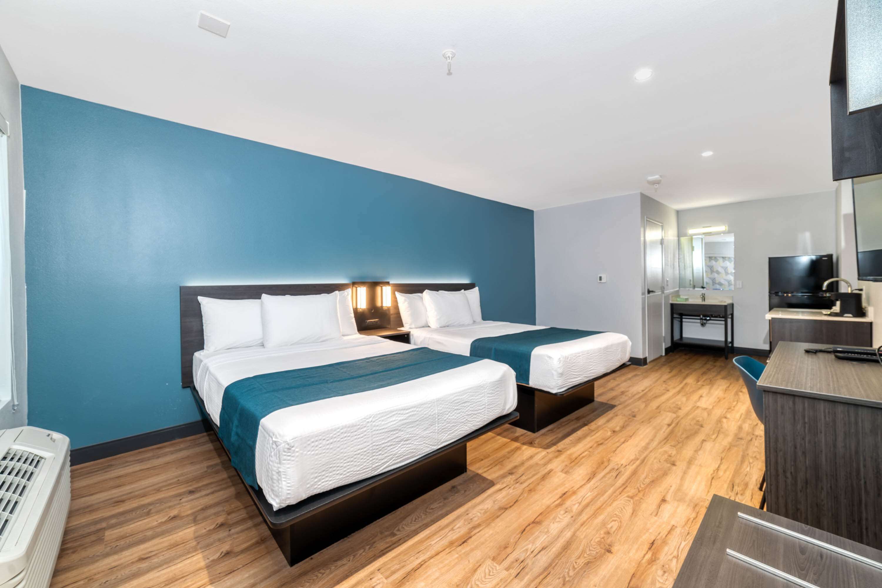 Quarto de hotel com duas camas, uma escrivaninha, um espelho e uma televisão.