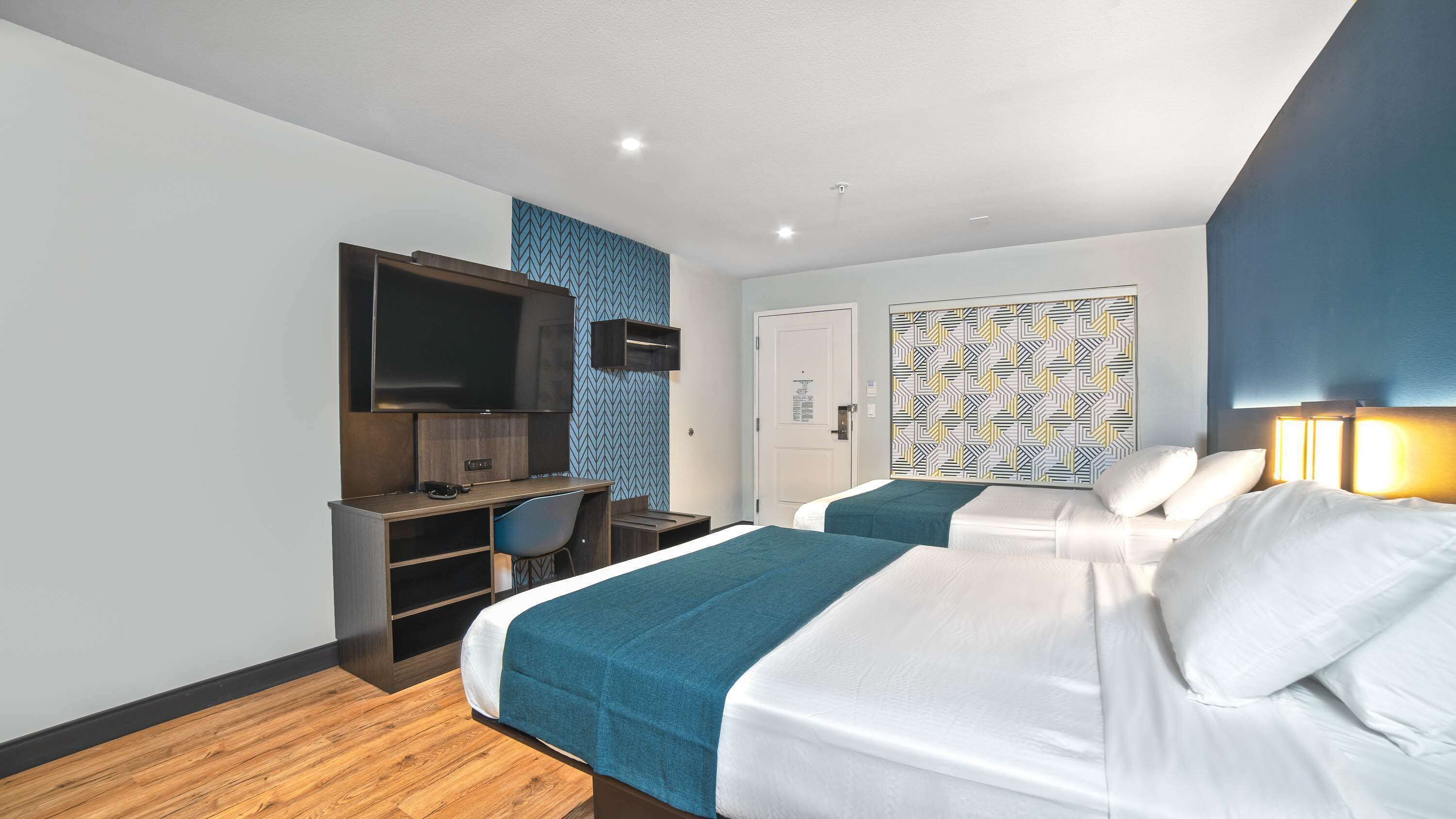 Ein Hotelzimmer mit zwei Betten, einem Schreibtisch, einem Fernseher und einer Wand mit Muster.