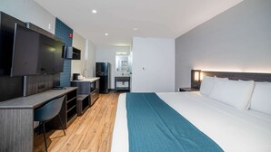 A hotel room with a bed, a desk with a chair, a television, a small kitchenette, and a bathroom. - Studio 6 Suites – Stockton, CA – Waterfront (Stockton)