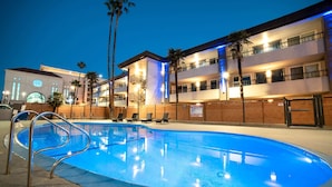A swimming pool with a metal ladder, lounge chairs, and palm trees. - Studio 6 Suites – Stockton, CA – Waterfront (Stockton)