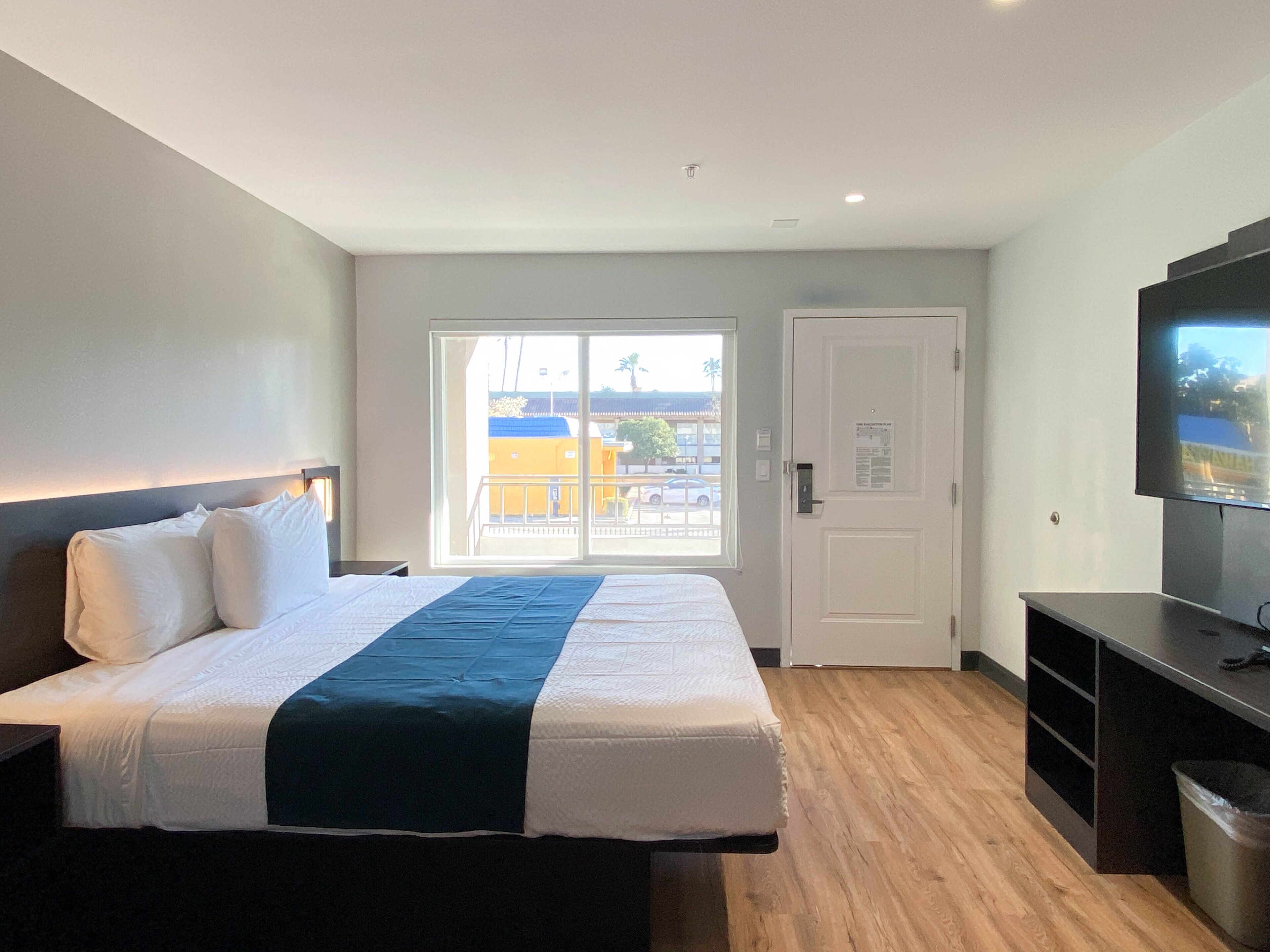 A hotel room with a bed, a television, a sliding door to the balcony, and a trash bin.