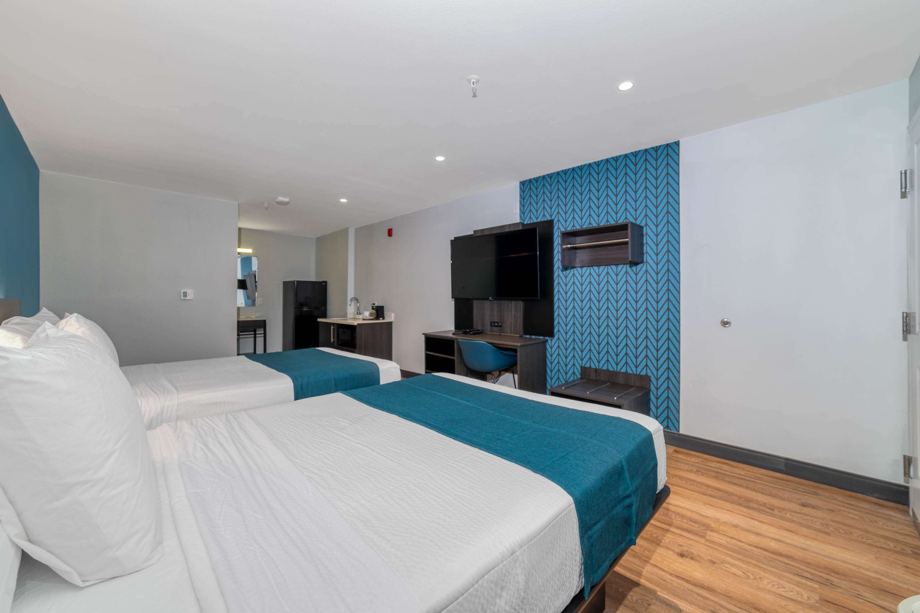 Een hotelkamer met twee bedden, een bureau, een stoel, een televisie en een blauwe, patroonrijke wand.