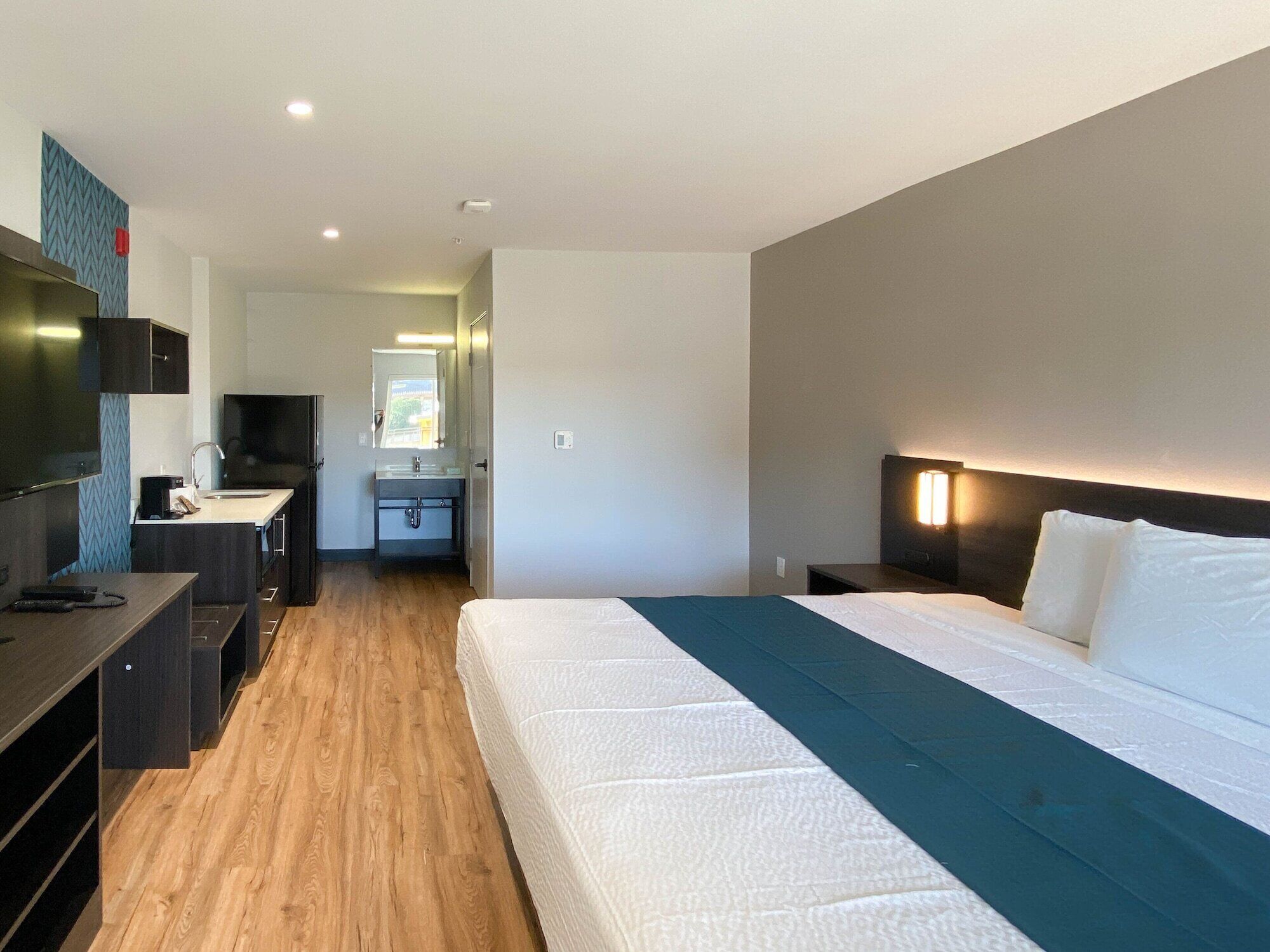 Una habitación de hotel moderna con una cama grande, televisor, escritorio y kitchenette.