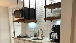 Une cuisine moderne avec des meubles blancs, un réfrigérateur en acier inoxydable, un four à micro-ondes et une machine à café.