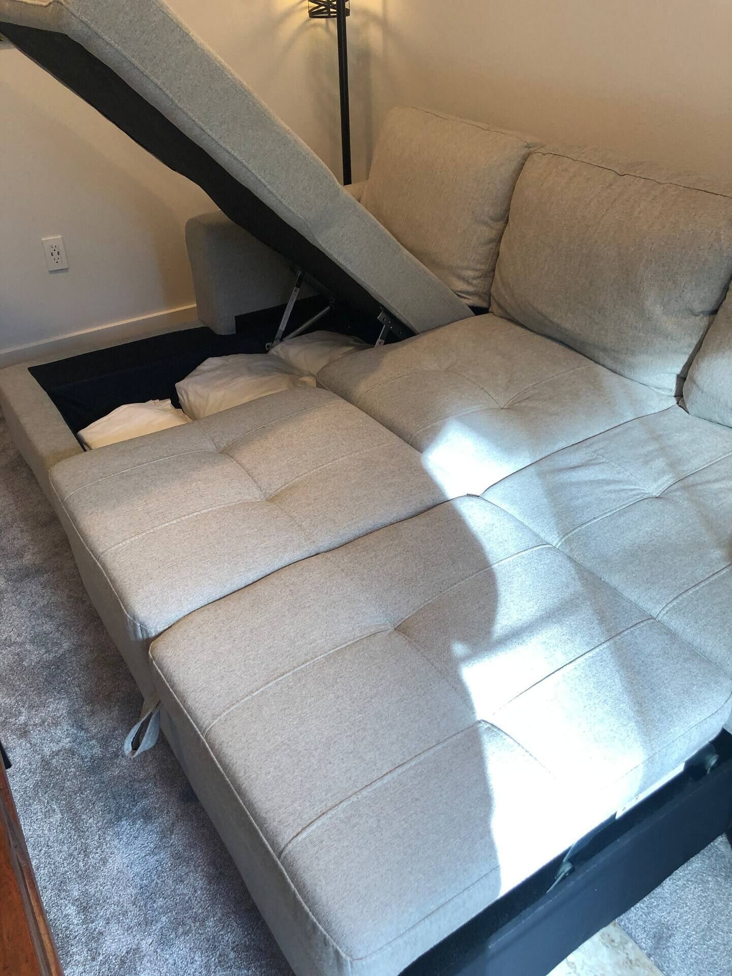 Ein Sofa mit Schlaffunktion in einem Zimmer mit Teppichboden und einer Stehlampe.