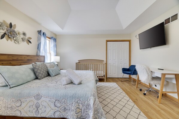 A bedroom with a bed, a desk, a chair, a crib, and a TV.