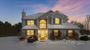 A two-story house with a snow-covered roof, a stone entrance, and a well-lit front door. - Private Heated Pool/Hot Tub/Huge Game Room/Sauna/Fire Pit/Huge Yard/3300 sq ft! (Stroudsburg)