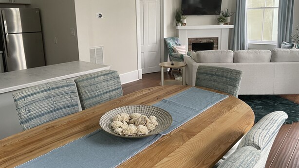 A modern living room with a wooden dining table, a sofa, and a television mounted above a fireplace. - By Forsyth Park, W/ King Bed +New Bath & Kitchen! (Savannah)