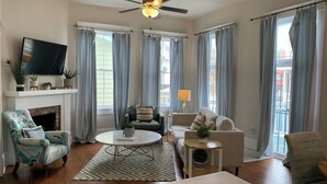 A living room with a fireplace, a ceiling fan, a television, and a sofa. - By Forsyth Park, W/ King Bed +New Bath & Kitchen! (Savannah)