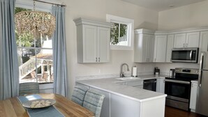 A modern kitchen with white cabinetry, a central island, stainless steel appliances, and a dining area with a wooden table and patterned chairs. - By Forsyth Park, W/ King Bed +New Bath & Kitchen! (Savannah)