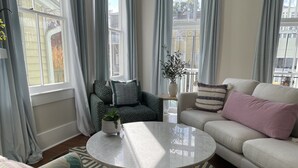 A living room with a round coffee table, a beige sofa, patterned armchairs, and a patterned rug. - By Forsyth Park, W/ King Bed +New Bath & Kitchen! (Savannah)