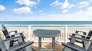 A deck with a table and two Adirondack chairs overlooking the ocean. - Dolphin Watch - 7Br - Oceanfront - Pool/Hot Tub (Kure Beach)
