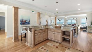 A spacious kitchen with a large island, wooden cabinets, and pendant lighting. - Dolphin Watch - 7Br - Oceanfront - Pool/Hot Tub (Kure Beach)