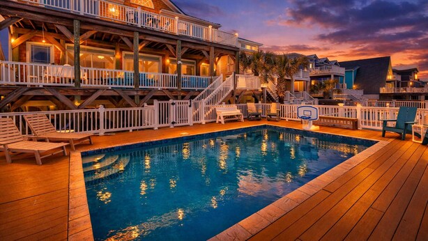 A pool area with a wooden deck, lounge chairs, and a basketball hoop. - Dolphin Watch - 7Br - Oceanfront - Pool/Hot Tub (Kure Beach)