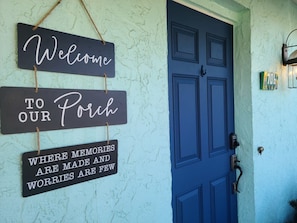 A blue door with a sign above it that reads "Welcome to our Porch" and another sign below it stating "Where memories are made and worries are few."
