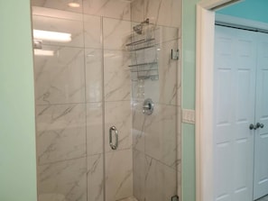 A bathroom with a glass-enclosed shower, a white door, and marble tiles.