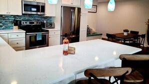 Une cuisine moderne avec des armoires blanches, des appareils en acier inoxydable, un grand îlot central et des luminaires suspendus.