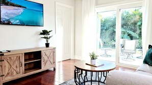 Un salon comprenant un meuble en bois, une table ronde, un canapé et une grande fenêtre donnant sur un paysage verdoyant.