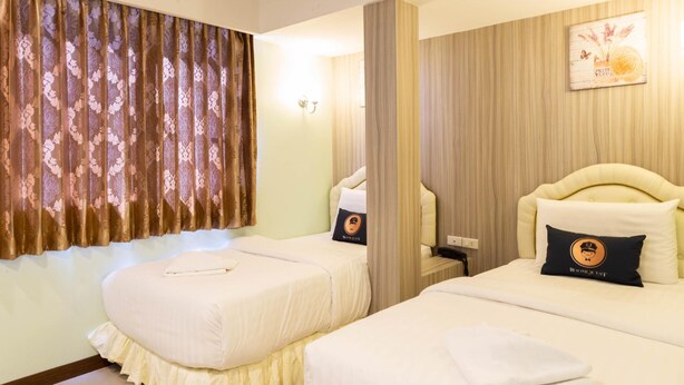 Habitación de hotel con dos camas, un ventanal con cortinas, una lámpara de pared y un cuadro enmarcado.