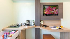 Habitación de hotel con un escritorio de madera, un televisor de pantalla plana en la pared, un espejo pequeño y un banco.